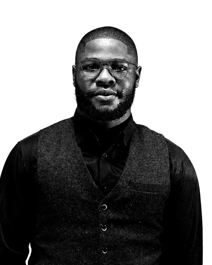 Black and white portrait of Caleb Kalu in glasses, a dark waistcoat and black shirt